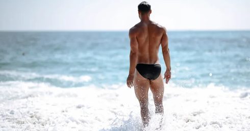 Athletic Guy in a Black Bikini at the Edge of the Ocean