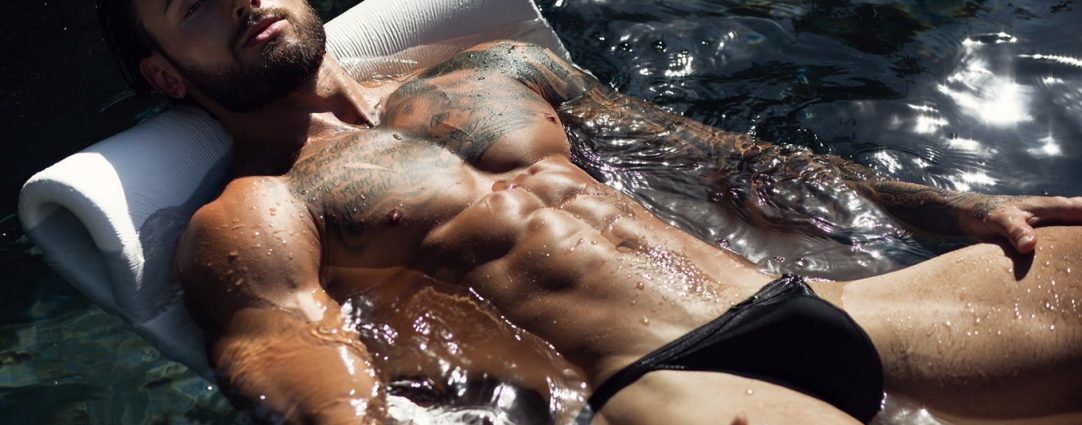 Muscular Stud in a Black Bikini Floating in a Pool